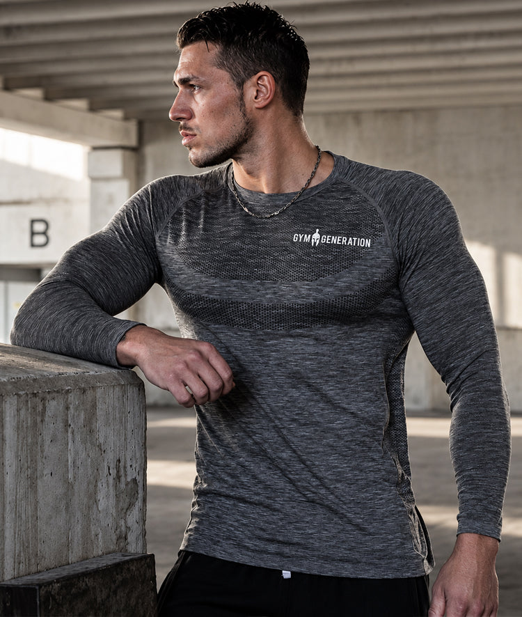 Mann lehnt seitlich an einer Betonwand, dunkelgraues Sportshirt mit langen Ärmeln