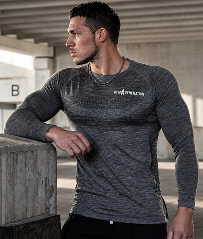 Mann lehnt seitlich an einer Betonwand, dunkelgraues Sportshirt mit langen Ärmeln
