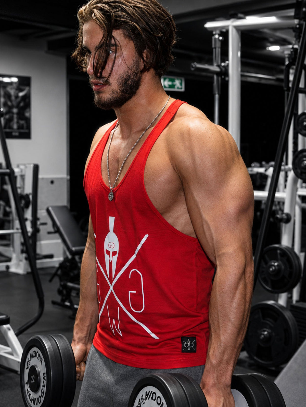 Athlet im roten Muskelshirt mit Kurzhanteln im Gym